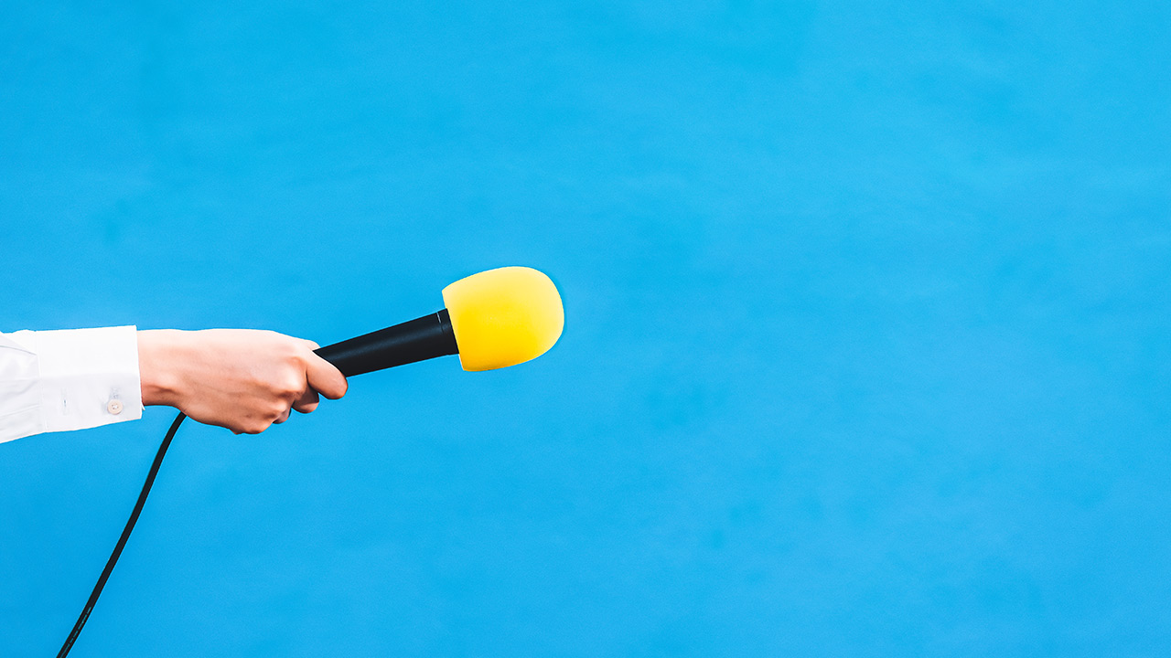 Weibliche Hand hält ein gelbes Mikrofon ins Bild
