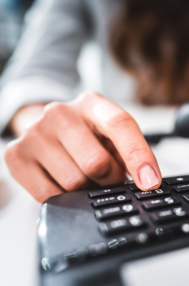 Hand wählt eine Telefonnummer auf einem Festnetztelefon